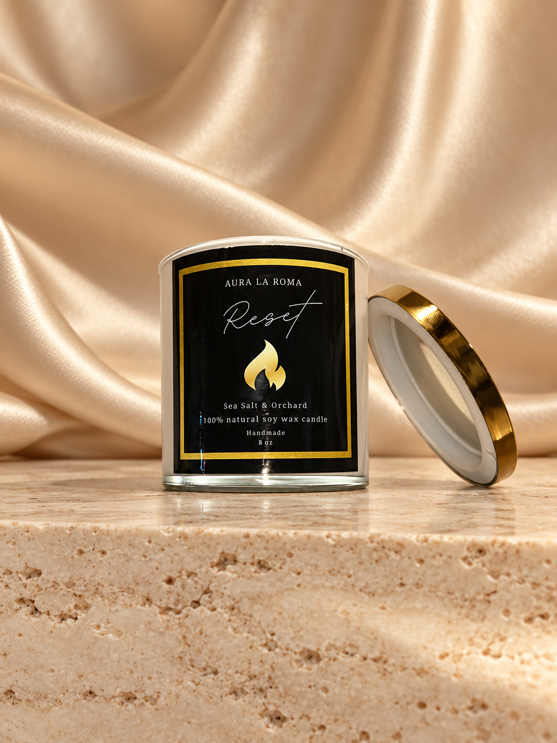 Aura La Roma Reset candle with gold lid against champagne satin on cream travertine.