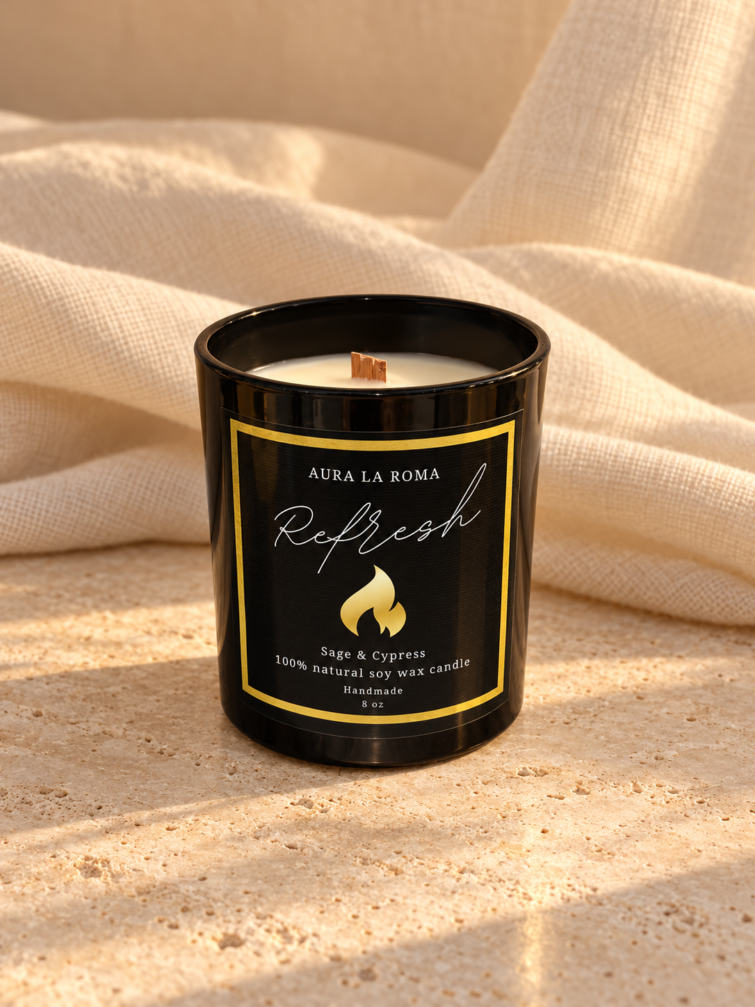Refresh Sage & Cypress black candle without lid, showing white wax and wooden wick in a warm linen and stone setting.