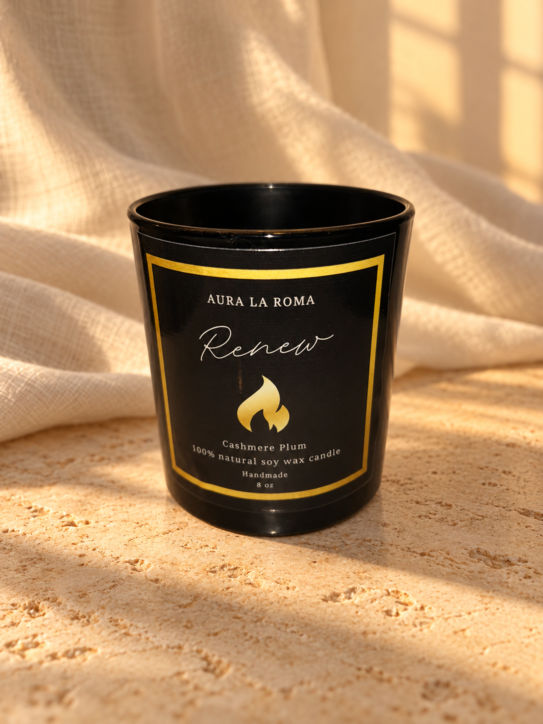 Renew Cashmere Plum black candle, front view, with warm ivory linen and natural stone.