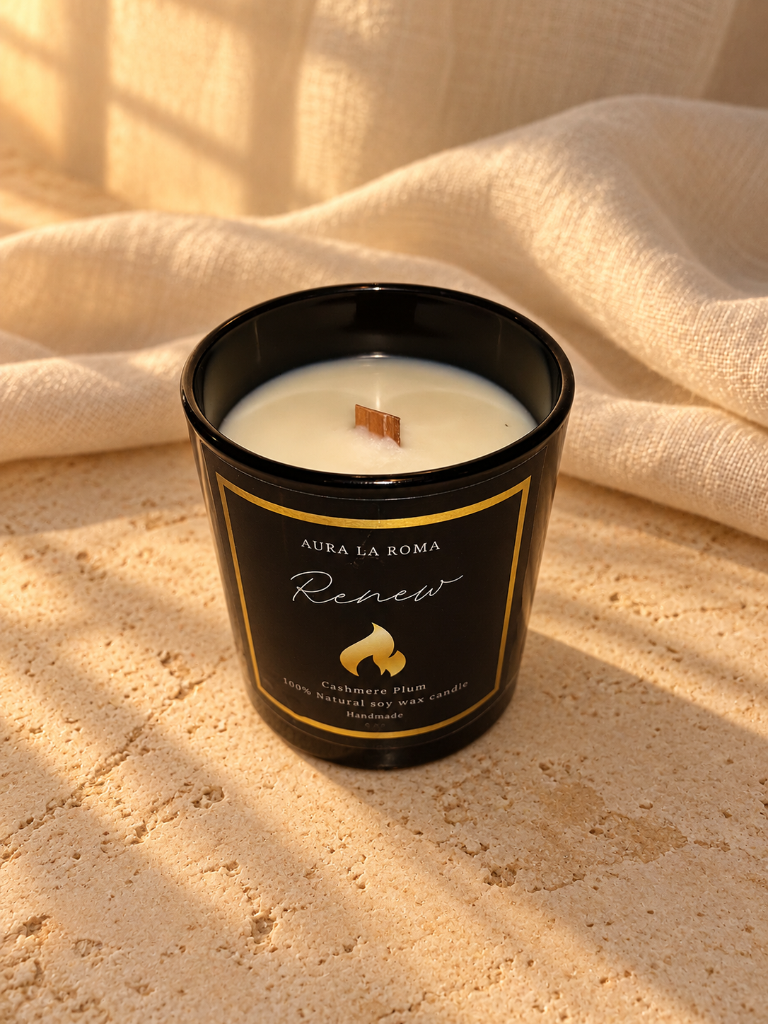 Renew Cashmere Plum black candle, top view, with warm ivory linen and natural stone.