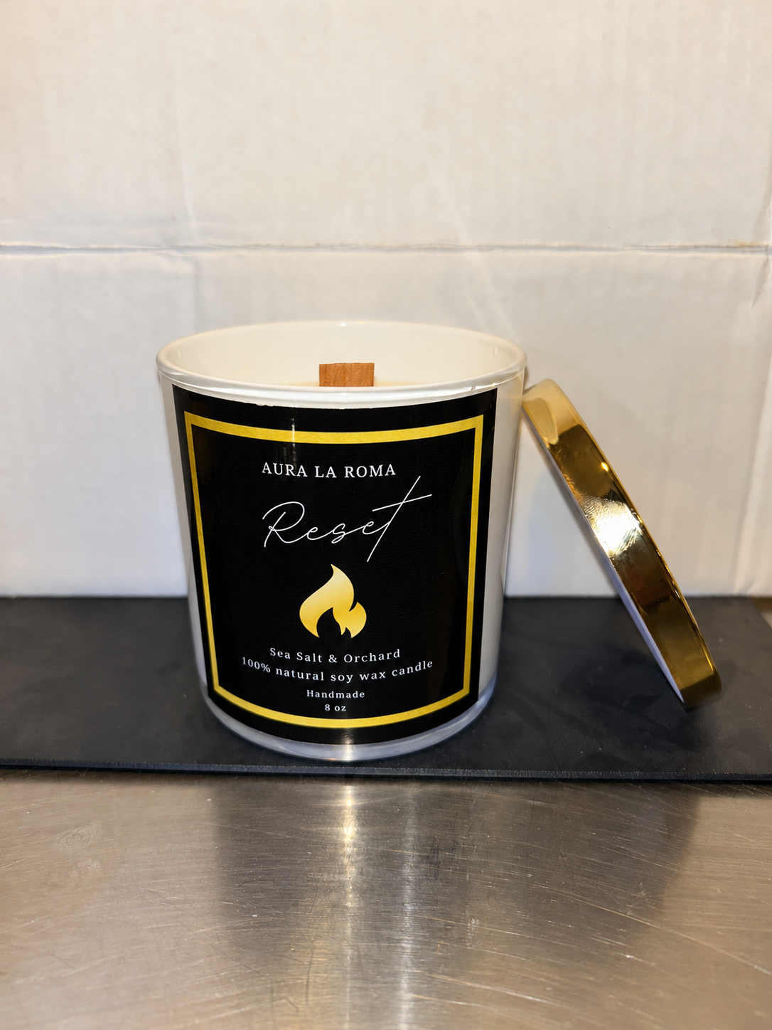 Reset candle with wooden wick and gold lid alongside, with blue reflection removed.